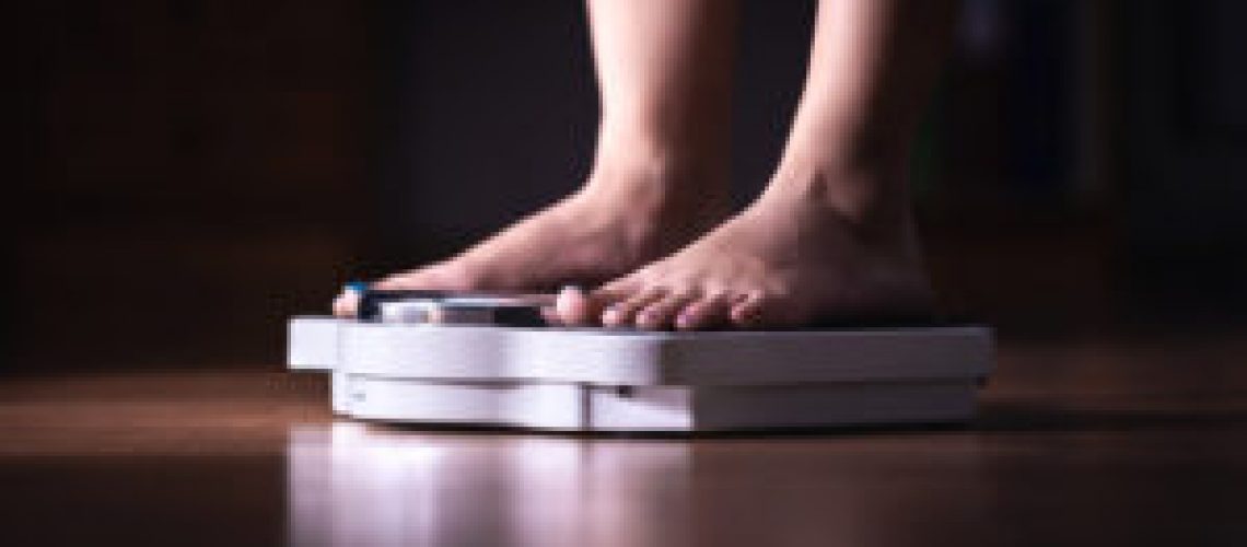 Feet on scale. Weight loss and diet concept. Woman weighing herself. Fitness lady dieting. Weightloss and dietetics. Dark late night mood.
